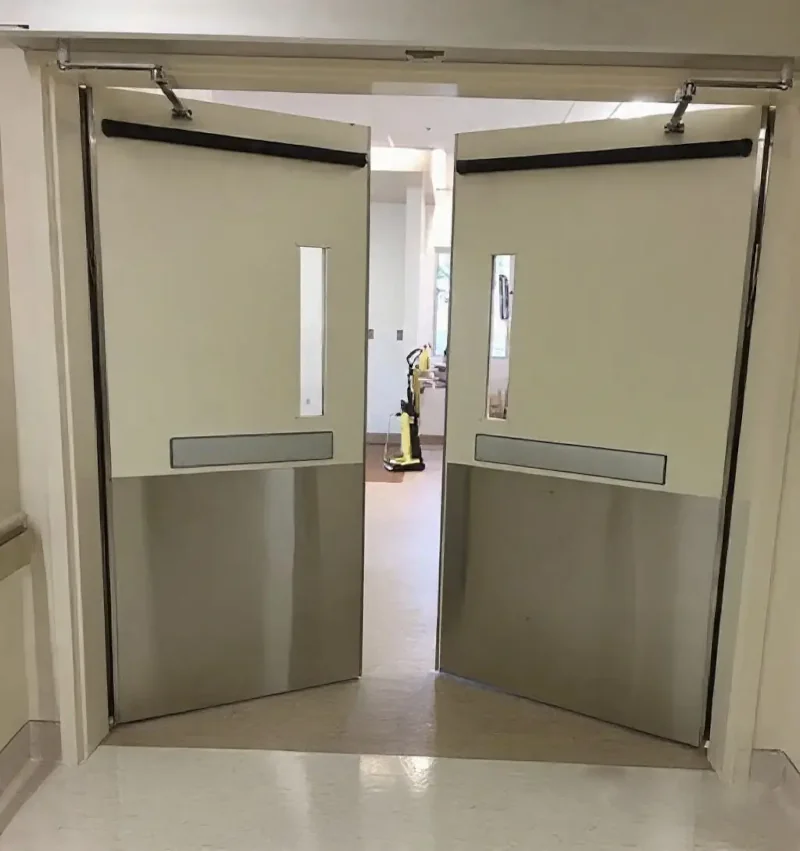 Teal heavy-duty double swing doors with vision panels and stainless steel kick plates in a sterile hospital corridor.