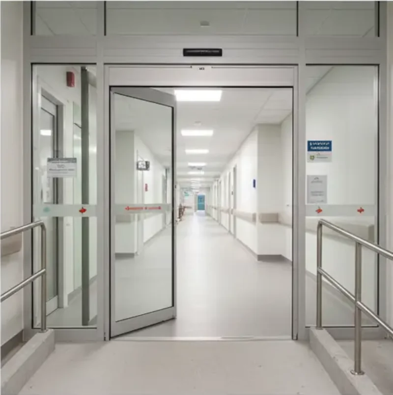 Automatic glass pedestrian door with overhead motion sensors and accessibility handrails at a modern clinic entrance.